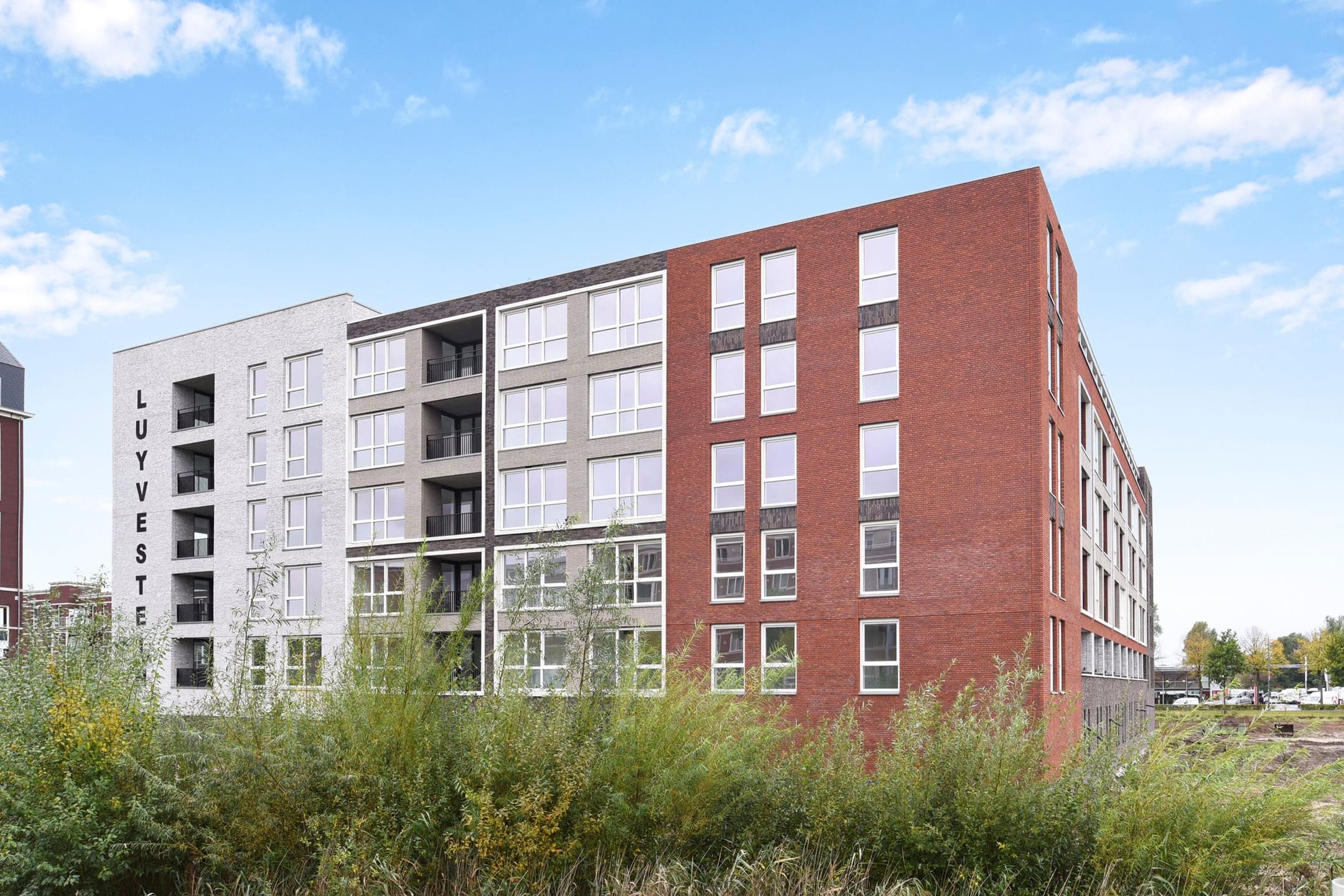 Het appartementengebouw Waterburcht W3 met gevels van rode, grijze en lichte baksteen, gezien over het riet.